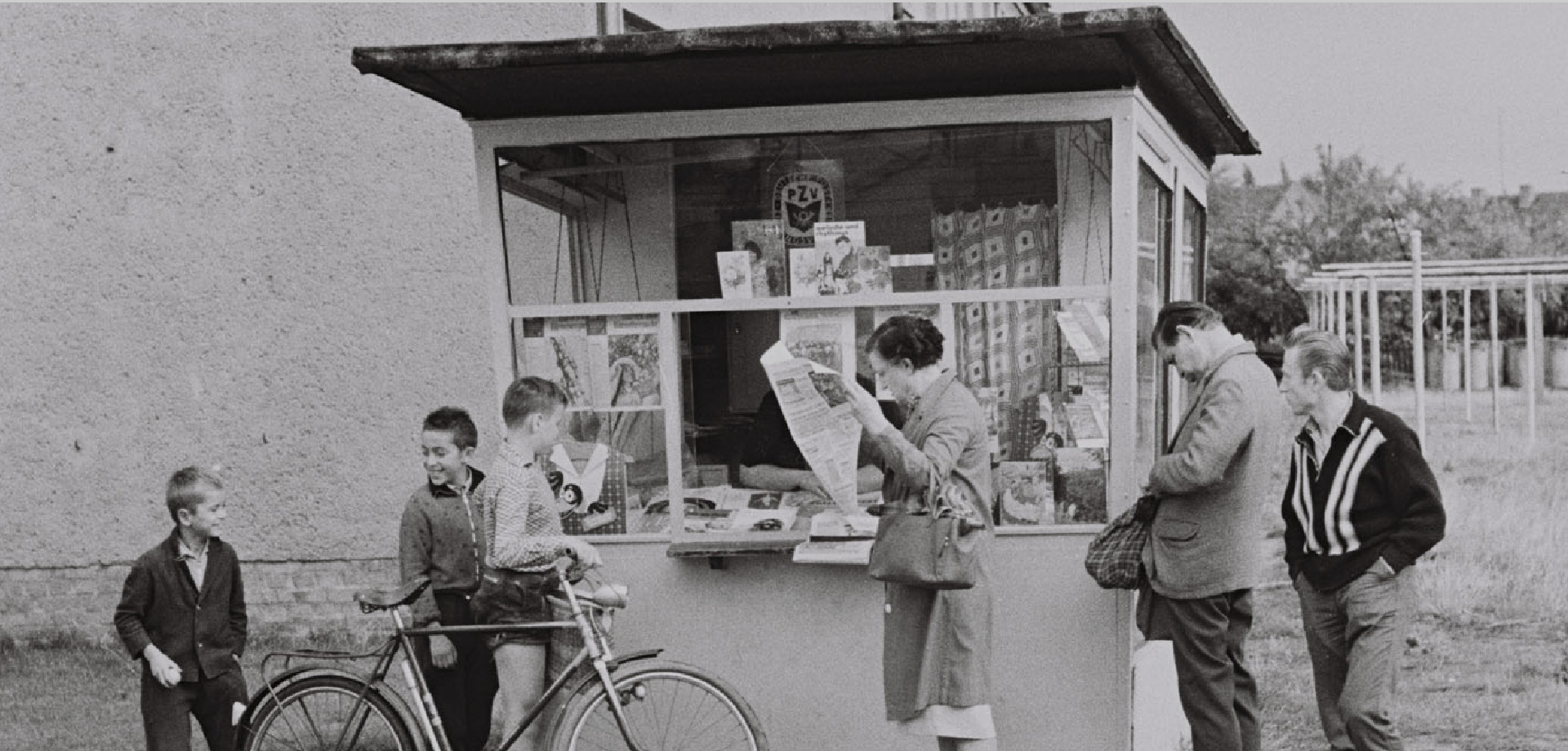 Ein Kiosk vor dem Menschen stehen, Erwachsene und Kinder. Eine Frau liest Zeitung